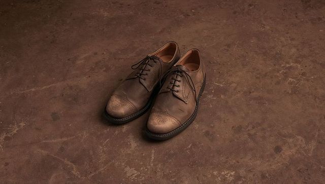 Worn brown leather brogues sitting on rustic workshop floor showing tied laces and scuffs