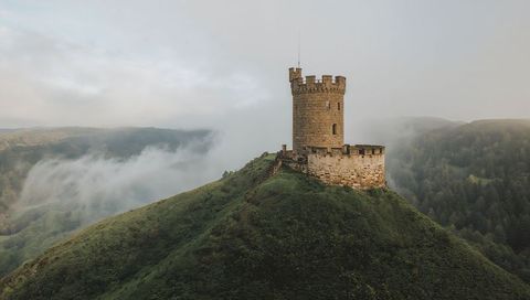 Misty medieval stone tower crowning lush hilltop with crenellated battlements and path