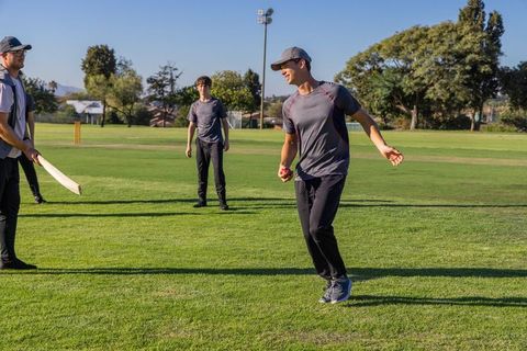 Young cricketers practicing bowling and batting on green club field under clear blue sky
