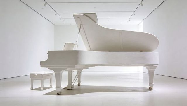 White grand piano showcasing raised lid and bench in minimalist gallery interior
