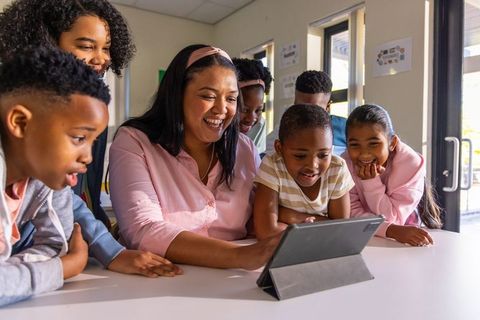 Teacher guiding diverse elementary students around tablet, collaborative digital learning