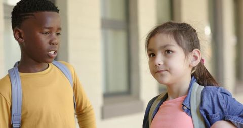 Elementary students talking and listening in school hallway with backpacks and casual jackets