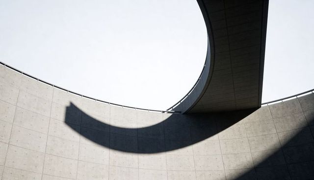 Curved concrete atrium with circular oculus and elevated walkway casting dramatic shadow