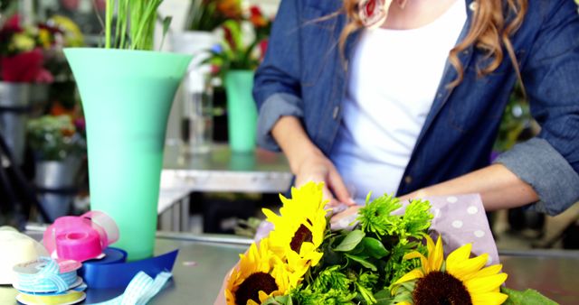 Female florist arranging a vibrant sunflower bouquet in a flower shop, surrounded by tools and ribbons, ideal for illustrating a day in the life of a florist, small business, creative workspaces, summer floral themes, and fresh flowers.