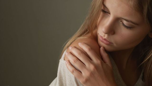 Contemplative teenage girl holding shoulder looking down soft light minimal portrait