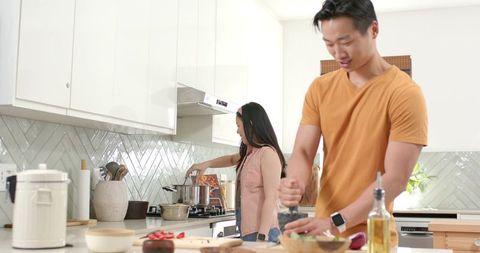 Asian couple cooking together in bright modern kitchen, chopping vegetables and stirring pot