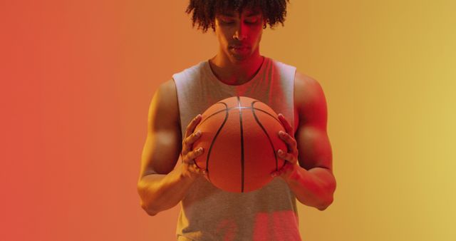African American man holding basketball with intense focus standing in front of vibrant gradient background. Great for fitness inspiration, sports advertisements, training guides, or athletic apparel promotions.