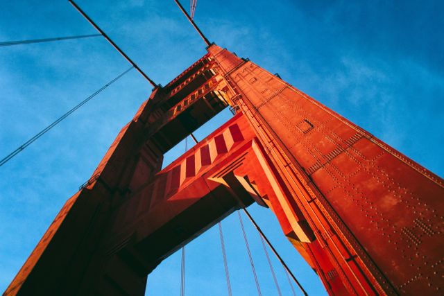View looking up at the tower of the Golden Gate Bridge highlighting its vibrant red color against the clear blue sky. Ideal for travel brochures, architectural studies, tourism advertisements, and content related to San Francisco landmarks.