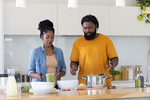 African american couple cooking, chopping tomatoes and stirring in bright modern kitchen