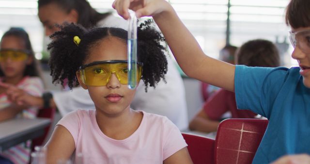 Children working in school laboratory engaged in chemistry experiment. Features young diverse kids, reinforcing the importance of STEM education including a girl in focus wearing safety goggles while another child holds a test tube. Ideal for educational content, STEM promotion, school brochures, science program advertisements.