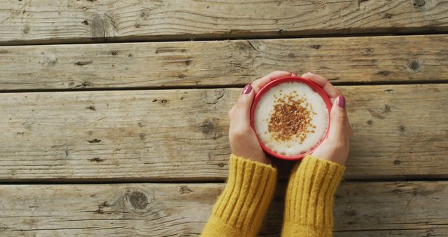 Image of hands of caucasian woman holding mug with coffee on wooden surface. seasons, autumn, coziness and relax concept.