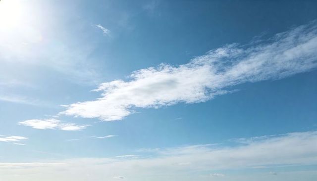 Elongated Cirrus Cloud Band Stretching Across Clear Blue Sky with Soft Sun Glare Minimalist Calm