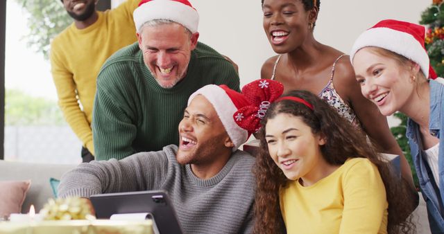 Happy group of diverse friends using tablet for image call at christmas party. Spending quality time at home together at christmas.
