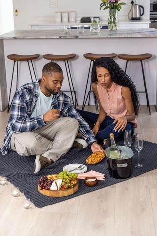Couple having cozy indoor picnic on kitchen floor with charcuterie, wine and candles