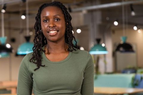 African american woman smiling in modern coworking space wearing olive top and gold chain
