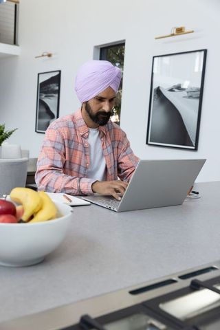 Indian man with lavender turban using laptop in modern kitchen