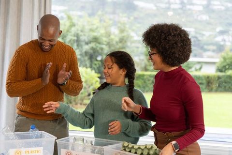 Multiracial family sorting recyclables and celebrating small eco wins at window table