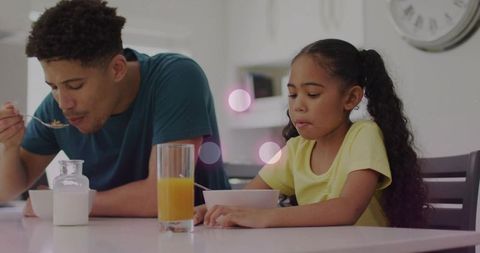 Father and daughter eating breakfast together in minimalist kitchen with orange juice