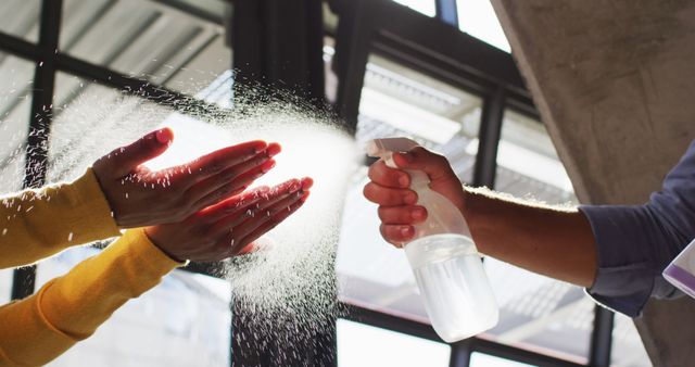 This image depicts close-up of hands being sanitized with spray bottle indoors, highlighting importance of hygiene and disinfection. Perfect for articles, blogs, and marketing materials focusing on health, hygiene, and sanitation measures, particularly in context of Covid-19 prevention efforts. Applicable for use in educational content, workplace safety guides, and promoting cleanliness practices.