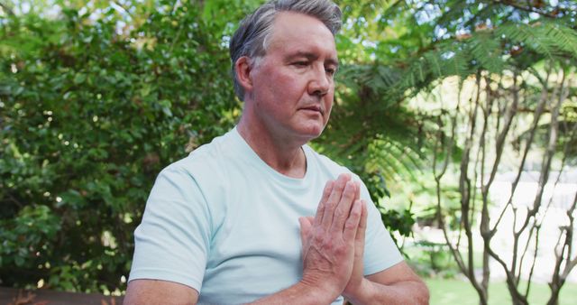 Senior caucasian man practicing yoga sitting in lotus position stretching and meditating in garden. healthy retirement lifestyle.