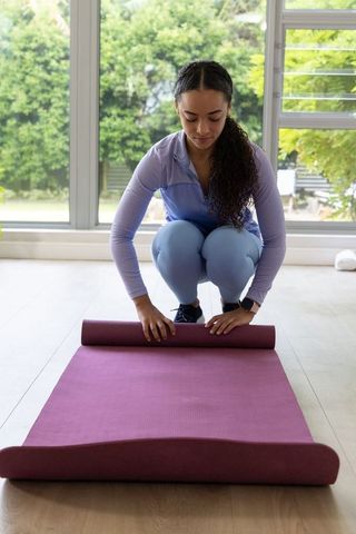 African american woman rolling purple yoga mat in sunlit home studio preparing workout