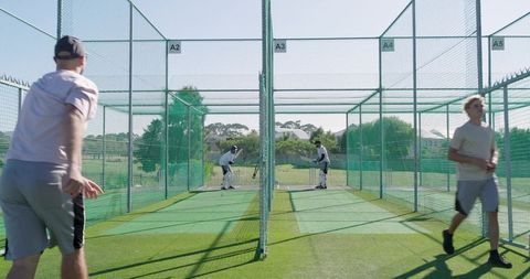 Cricket players practicing in outdoor net lanes with coach guiding batting drills