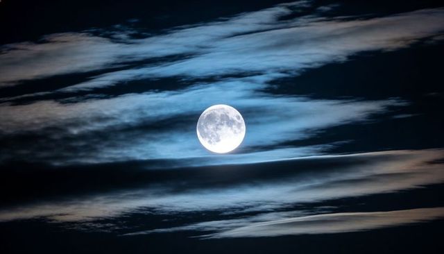 Full moon casting cool blue glow through layered clouds, cinematic nocturnal sky