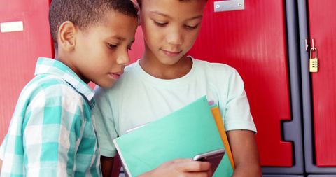 Boys Sharing Mobile Phone Near School Lockers Smiling