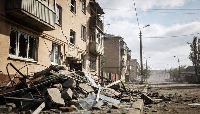 Rubble blocking residential street with damaged apartment facades, broken windows, dust