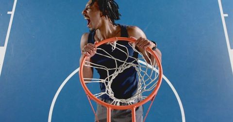 Energetic basketball player hanging on the hoop on blue court