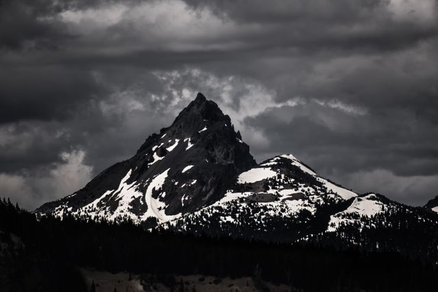 This image shows a majestic snow-capped mountain under a dramatic cloudy sky, ideal for themes related to nature, wilderness, and adventure. Perfect for use in outdoor magazines, travel websites, and advertisements for winter gear. It evokes a sense of rugged beauty and solitude, suitable for inspiration and motivational posters.