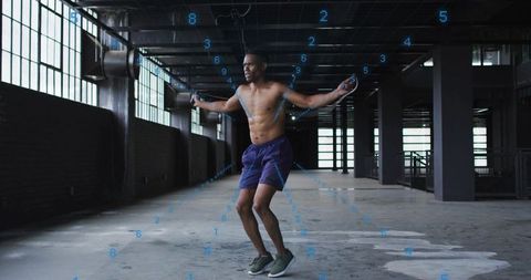 Shirtless athlete skipping rope inside industrial warehouse high-intensity cardio training