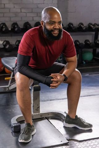 Smiling man resting on bench after strength training with dumbbells and smartwatch