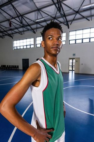 African american basketball player standing hands on hips on indoor court looking focused