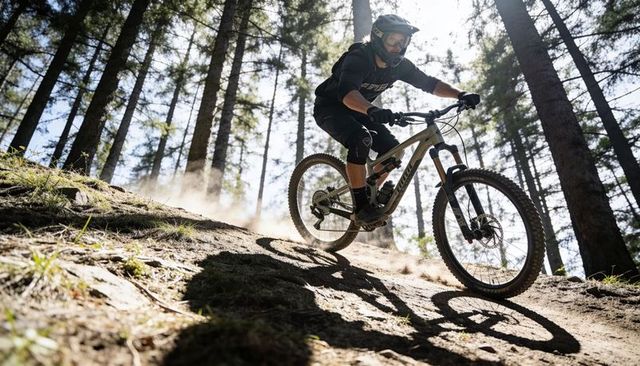 Male mountain biker descending steep pine forest trail kicking up dust with helmet and goggles