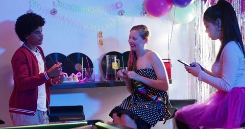 Diverse friends celebrating with neon balloons, polka-dot dress and retro vinyl decor
