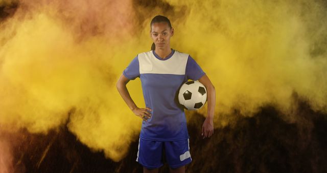 Digital composite image of Female soccer player holding a ball against smoke explosion in background. Sports fitness concept digital composite
