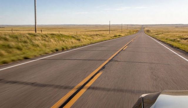 Endless prairie highway stretching toward horizon from moving car with double yellow line