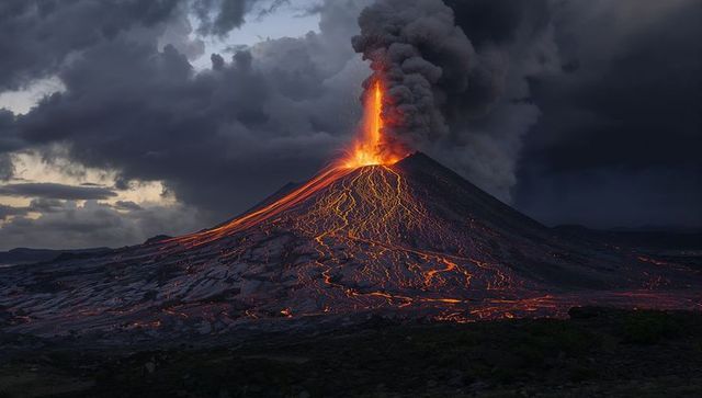 Erupting volcano at dusk with lava fountain and flowing molten channels