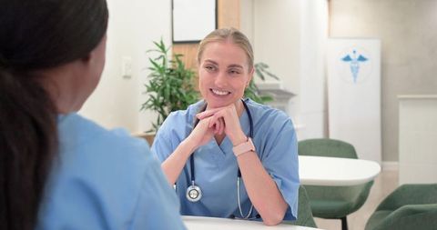 Smiling diverse nurses consulting at table holding stethoscope and collaborating in clinic