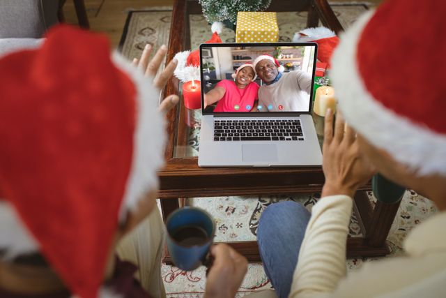 Diverse couple with santa hats having video call with happy african american couple. Christmas, celebration and digital composite image.