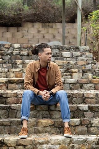 Contemplative african american man sitting on terraced stone steps wearing casual outfit