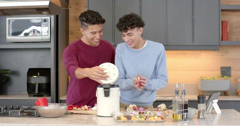 Friends cooking together in modern kitchen smiling while preparing vegetables