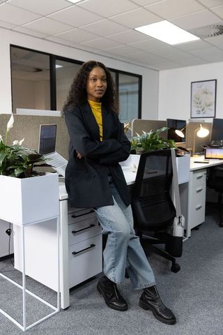 Young african american professional leaning against desk in modern open office