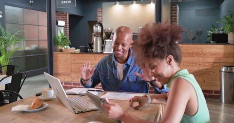 African american colleagues waving and laughing while collaborating over laptop and tablet