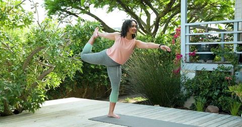 Woman practicing dancer pose on sunlit backyard deck, outdoor yoga, fitness lifestyle