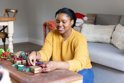 African american woman wrapping cozy holiday gifts with kraft paper ribbons and holly