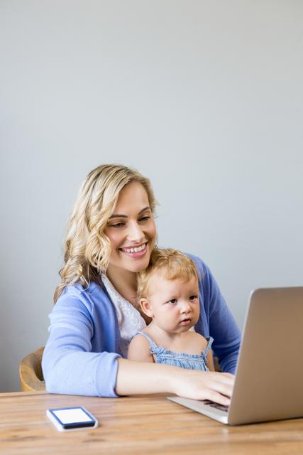 Mother and baby sitting at table and using laptop at home