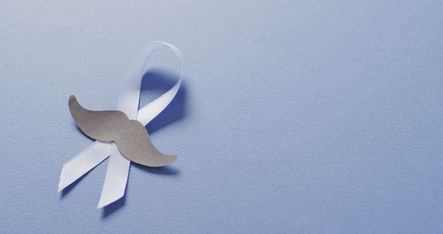 Image of paper moustache and pale blue prostate cancer ribbon on pale blue background. medical and healthcare awareness support campaign symbol for prostate cancer.