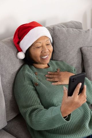 Smiling Asian Woman Taking Festive Selfie in Santa Hat on Sofa